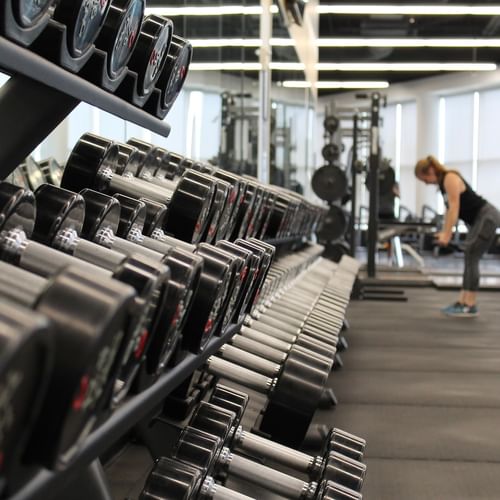 Neatly organized rack of dumbbells in gym, with a person lifting weights in the background at Pickalbatros Golf Beach Resort